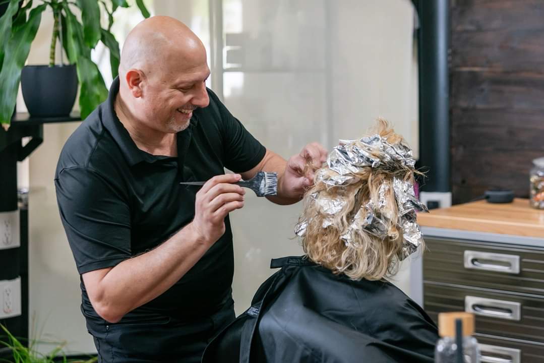 man smiling while putting foil highlights in blond women's hair